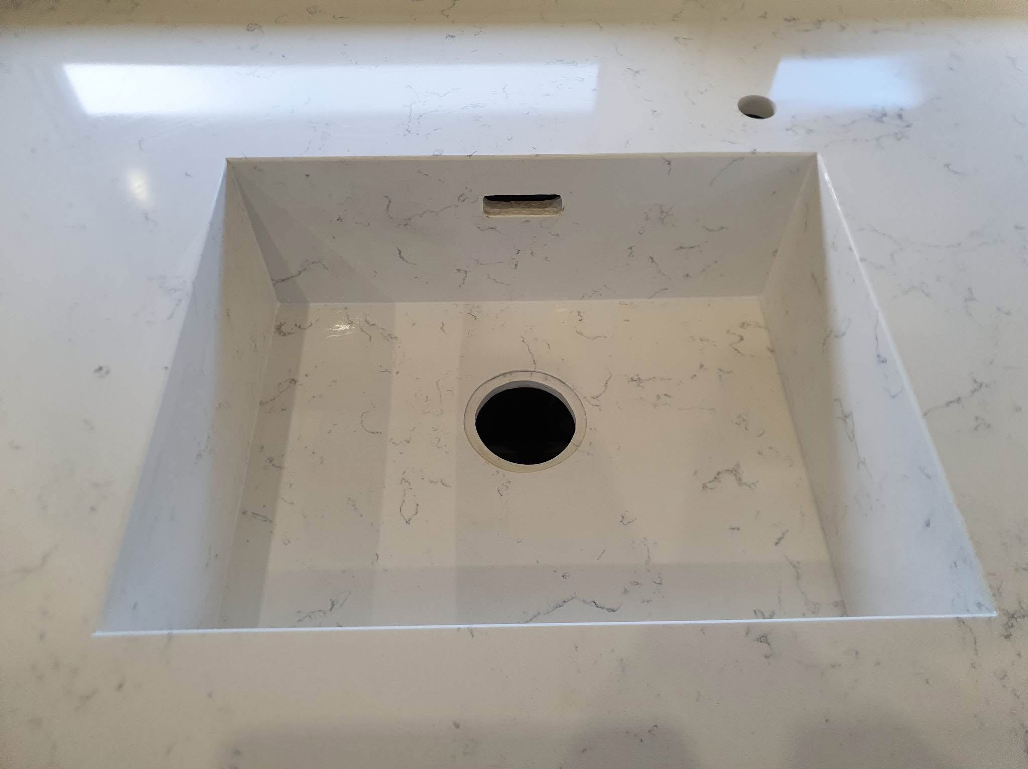 Biały blat kuchenny z konglomeratu kwarcowego ze zintegrowanym zlewem i otworem na baterię, widok z góry, gładka powierzchnia z delikatnym wzorem żyłek.