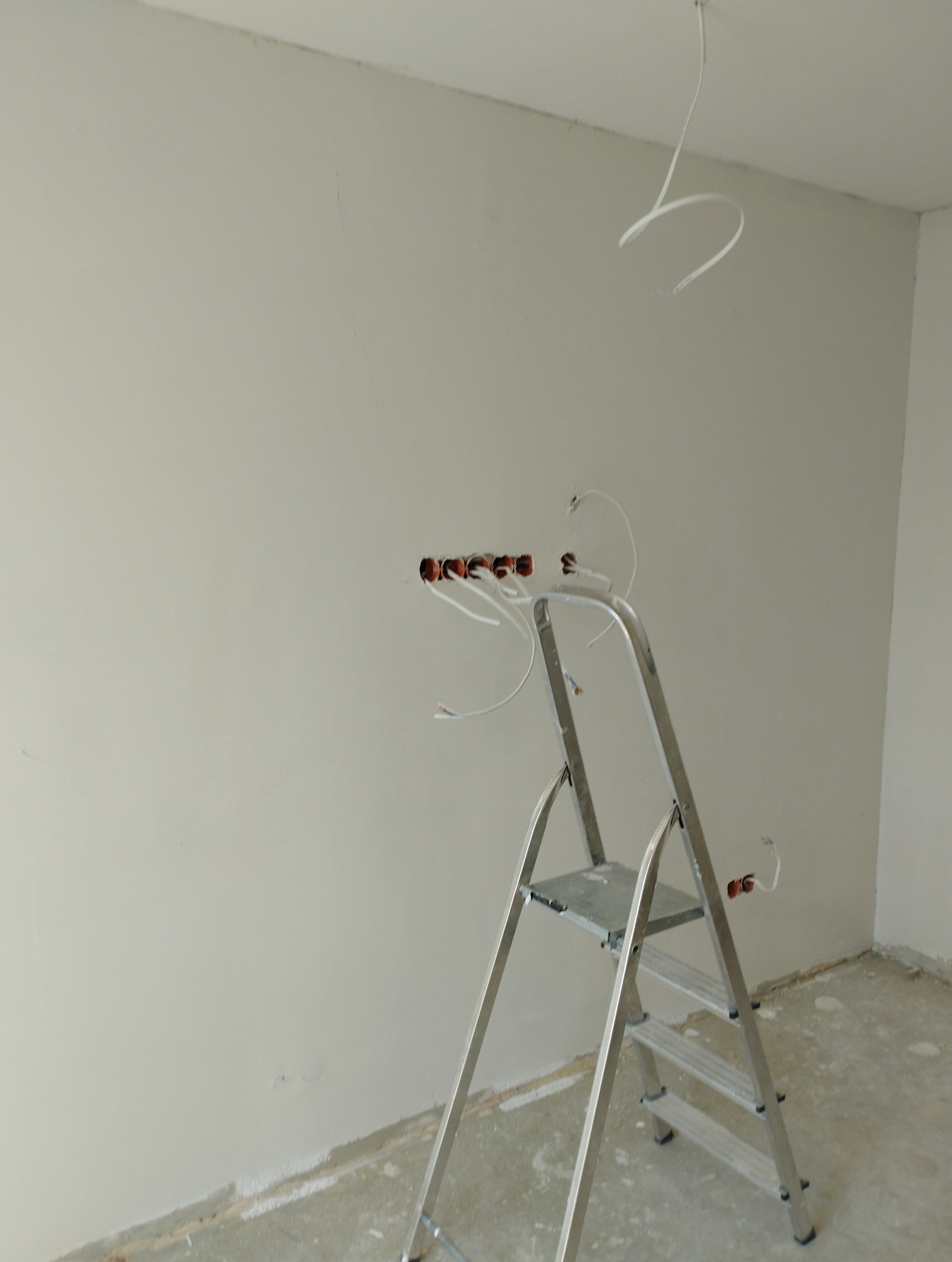 Pokój w trakcie remontu: ściany po szpachlowaniu, widoczne kable elektryczne i drabina aluminiowa. Przygotowanie do malowania ścian.