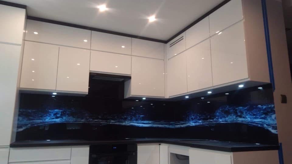 Błyszcząca, czarna ściana nad blatem kuchennym z motywem falującej wody w odcieniach błękitu, oświetlona punktowymi lampkami LED, w nowoczesnej kuchni z białymi szafkami.