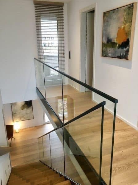 Nowoczesna balustrada szklana z czarnymi profilami na schodach w jasnym wnętrzu. Widok z góry, parkiet na podłodze, obraz na ścianie.