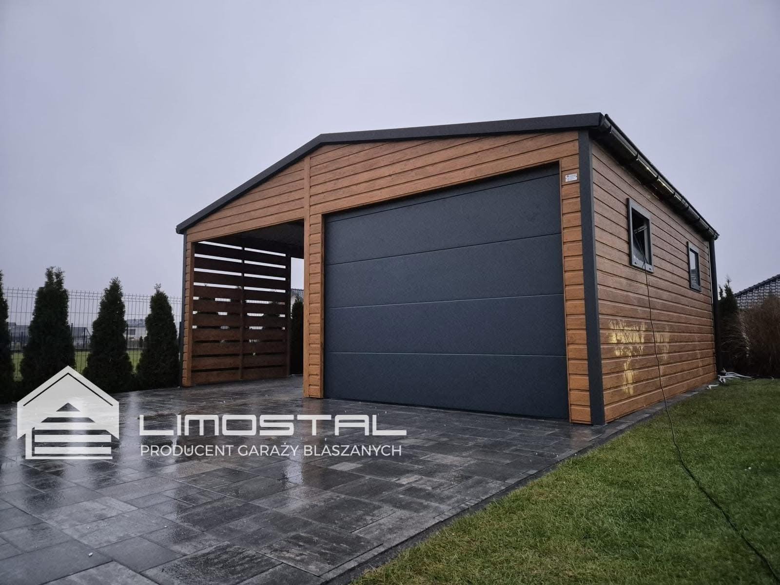 Nowoczesny garaż z brązową elewacją imitującą drewno i antracytową bramą segmentową, z zadaszeniem na samochód obok, kostka brukowa, logo producenta na pierwszym planie.