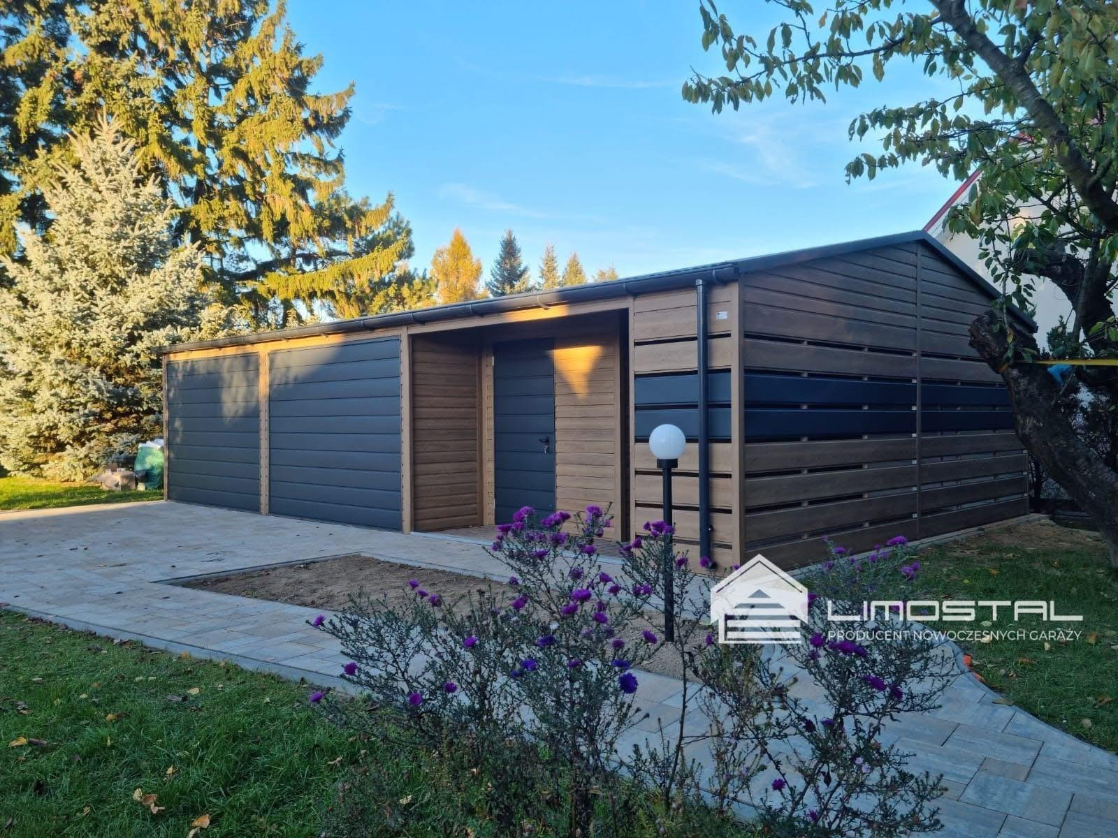 Nowoczesny garaż z elementami drewnopodobnymi i szarymi panelami, oświetlony lampą kulą, z widocznym logo producenta i fioletowymi kwiatami na pierwszym planie.