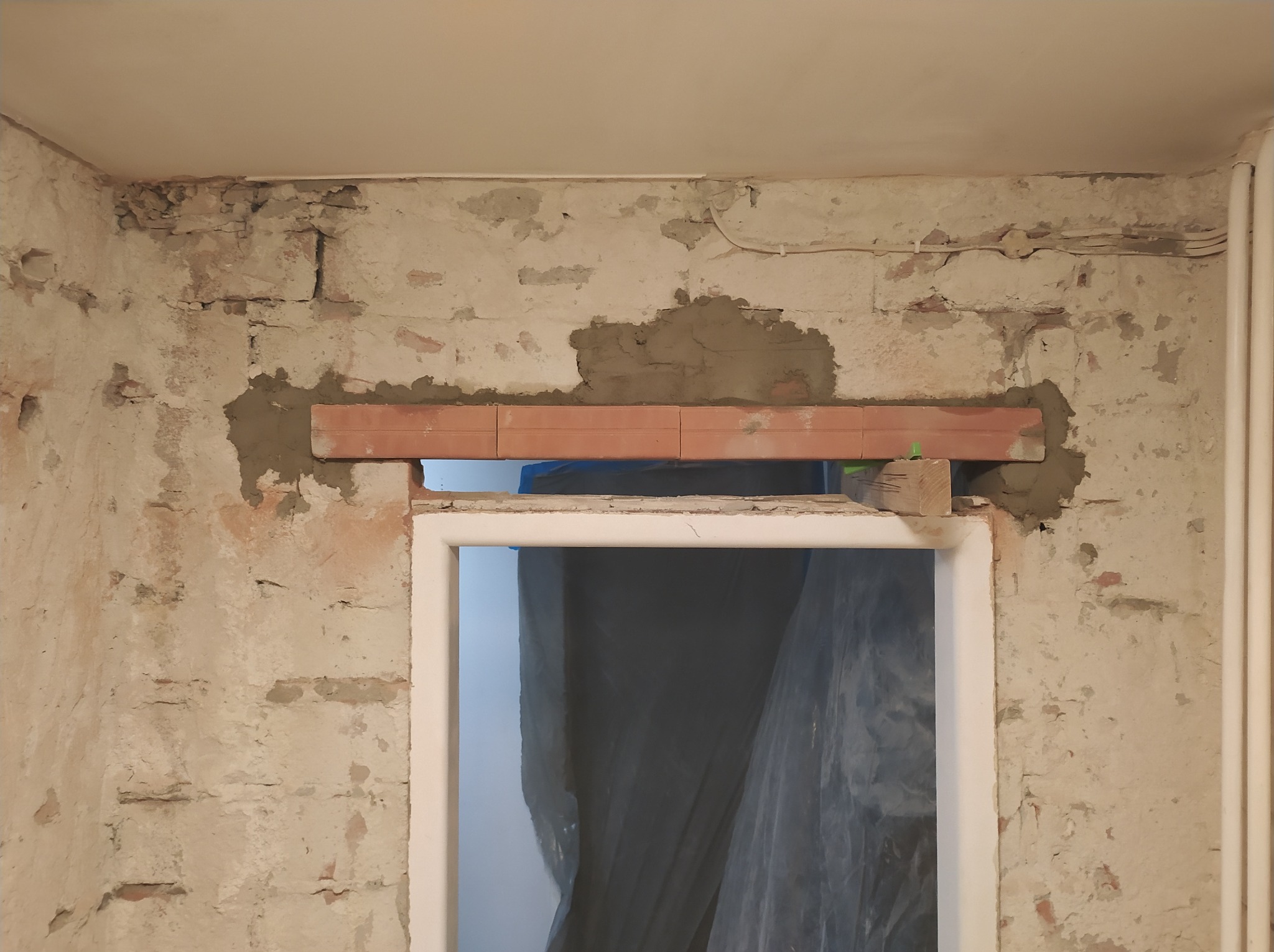 Przygotowanie otworu na drzwi: murowanie nadproża z czerwonej cegły na zaprawie w surowym, otynkowanym wnętrzu, widoczne ślady po starych instalacjach elektrycznych.