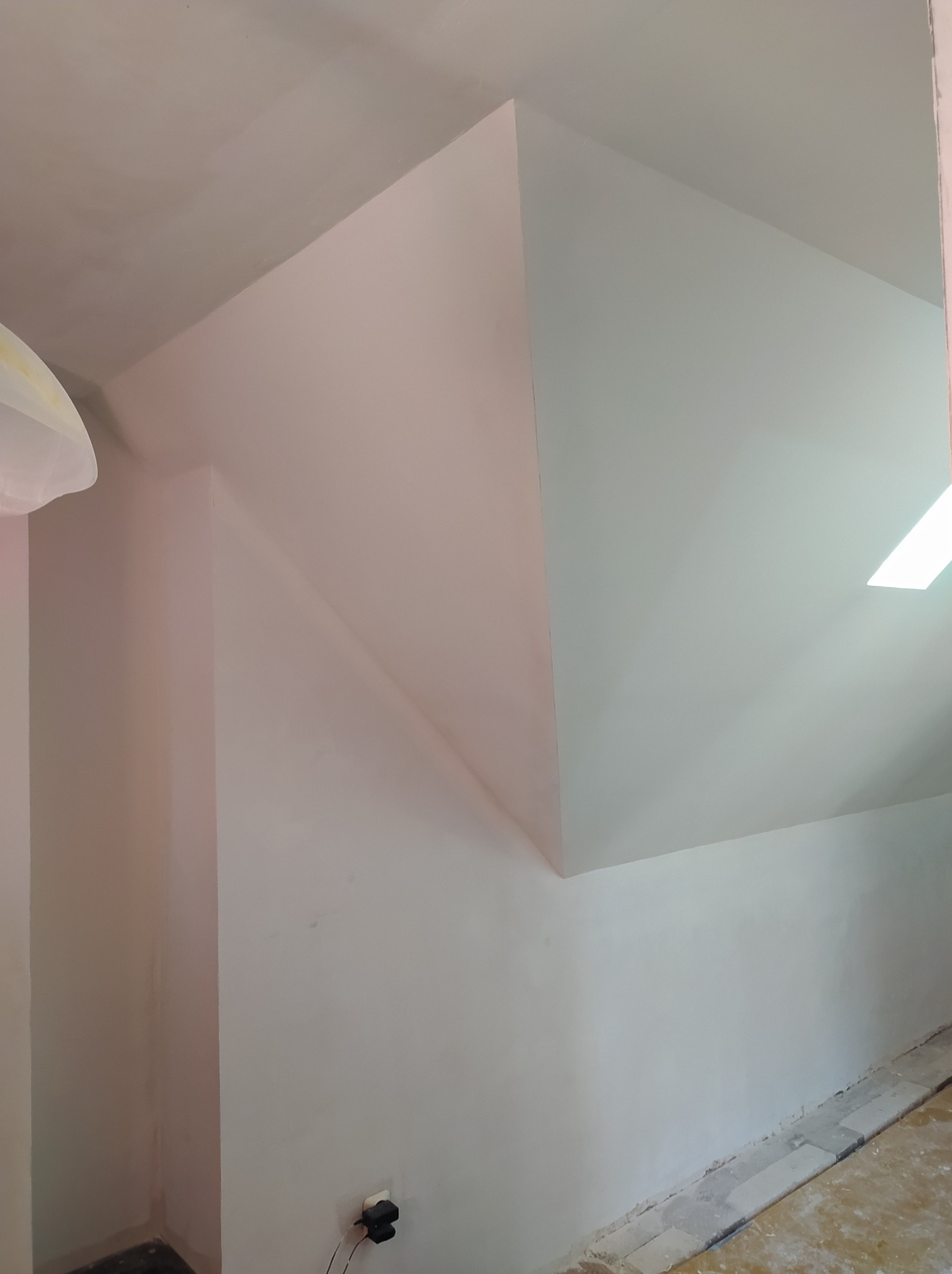 Ściana pod skosem po szpachlowaniu i malowaniu na dwa odcienie bieli, widoczne gniazdko elektryczne i fragment podłogi.