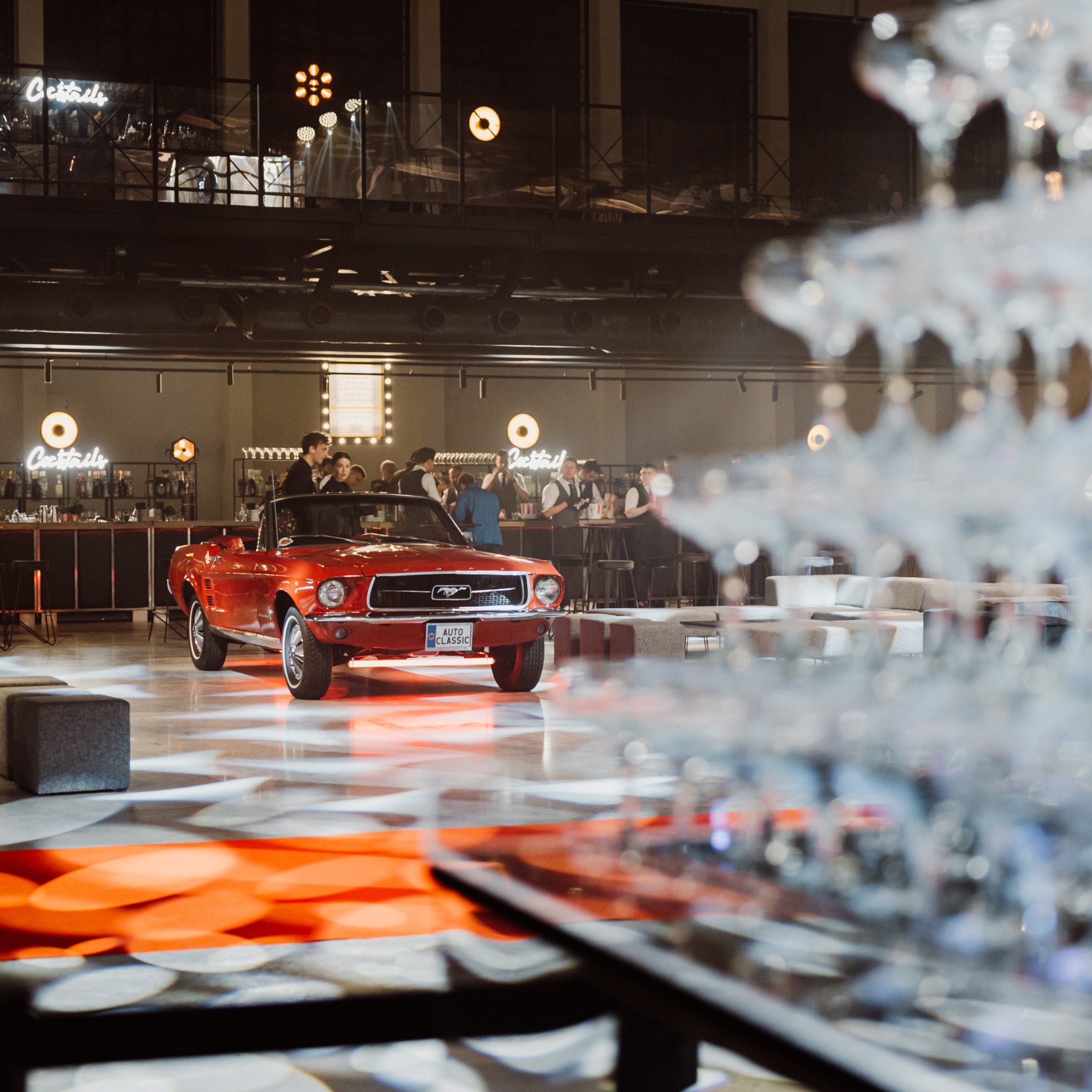 Czerwony kabriolet Mustang na błyszczącej podłodze, bar z napojami w tle, dekoracje i oświetlenie eventowe.