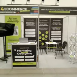 Stoisko targowe firmy Time 4 Ecommerce z ekspozycją usług: darmowy audyt sklepu internetowego, marketing kreatywny, automatyzacja procesów, projektowanie sklepów. Widoczny laptop, monitor, ulotki...