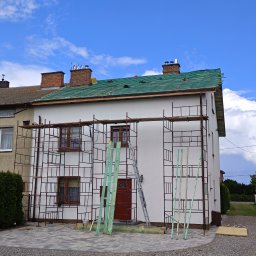 Ekspert-Dach Pogotowie Dekarskie - Dom w trakcie wymiany dachu, widoczne rusztowania, częściowo zdjęte stare pokrycie i przygotowane nowe elementy konstrukcyjne. Błękitne niebo w tle.