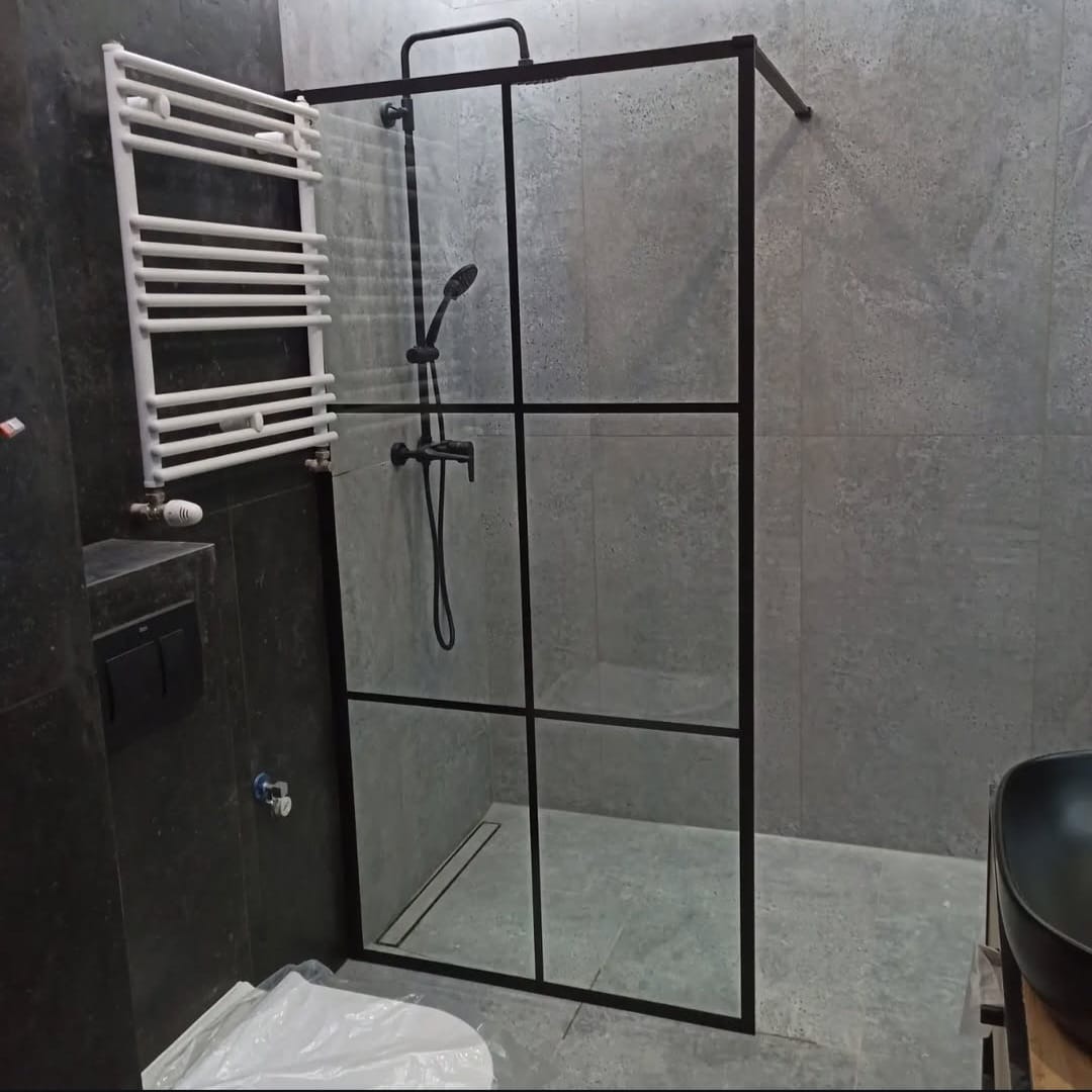 Nowoczesna łazienka z szarą płytką, kabiną prysznicową z czarnymi profilami, czarną armaturą i grzejnikiem drabinkowym w kolorze białym.