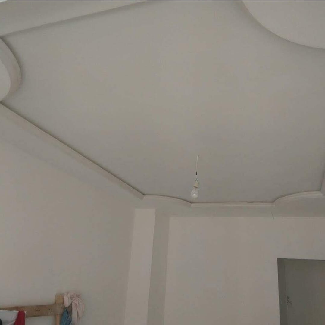 Pomieszczenie z wykończonym sufitem podwieszanym z dekoracyjnymi narożnikami i gołą żarówką zwisającą na kablu.