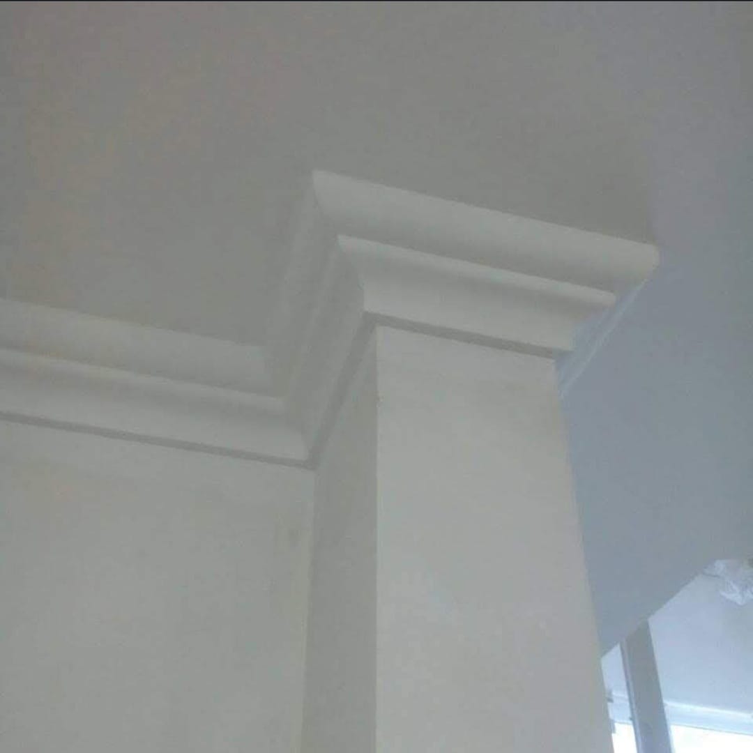 Biała kolumna z dekoracyjnym gzymsem na styku ściany i sufitu, widok od dołu, minimalistyczny design.