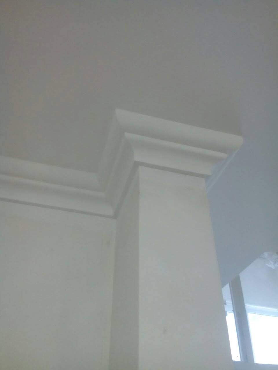 Biała kolumna z dekoracyjnym gzymsem przy suficie, widok z dołu, ściana z widocznymi niedoskonałościami malowania.