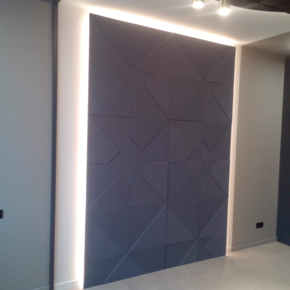Szara ściana dekoracyjna z geometrycznym wzorem 3D, oświetlona listwą LED, zrealizowana w mieszkaniu w Krakowie.