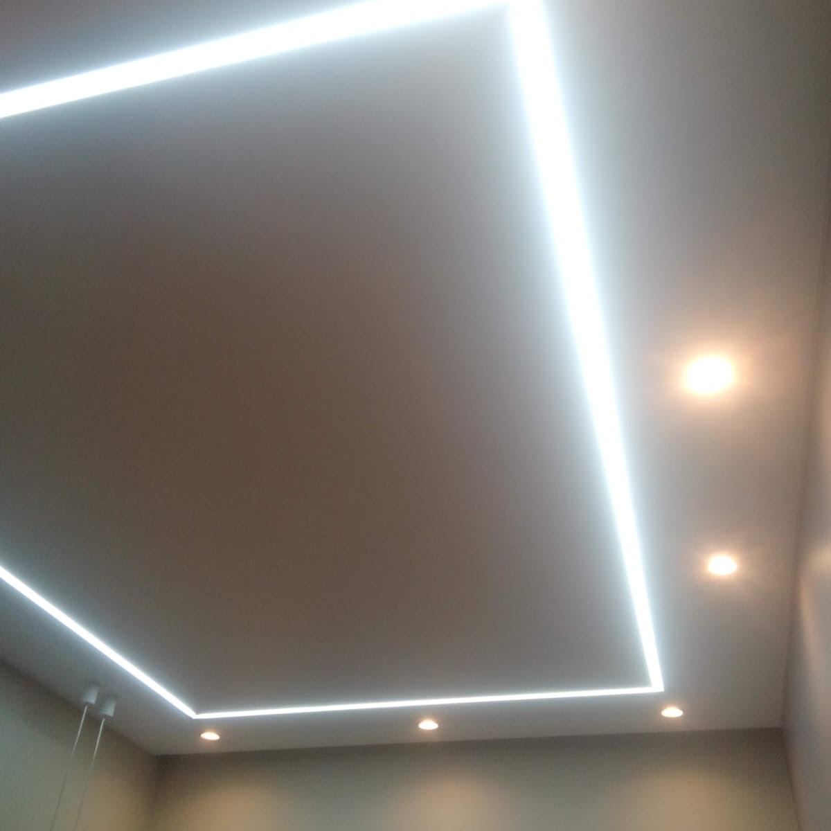 Minimalistyczny sufit podwieszany z oświetleniem LED w kształcie prostokąta i punktowymi lampami halogenowymi, widoczne przewody zasilające.