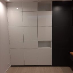 Da Vinci Sztuka Mebli - Biało-czarna zabudowa meblowa z błyszczącymi frontami, składająca się z kwadratowych modułów, z otwartymi półkami, oświetlona punktowo, na podłodze panele imitujące drewno.