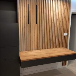 Da Vinci Sztuka Mebli - Nowoczesna zabudowa meblowa z drewnianymi lamelami na ścianie, czarnym biurkiem z szufladami i wiszącymi lampami cylindrycznymi.