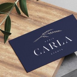 Digital Marketing, Branding, Key Visual - Elegancka wizytówka w granatowym kolorze z subtelnym logo roślinnym i napisem 'Carla Events' na drewnianym tle z gałązką. Minimalistyczny design.