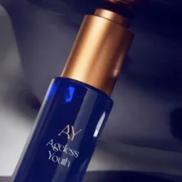 Elegancka, granatowa buteleczka serum 'AY Ageless Youth' z złotą pompką na błyszczącym, ciemnym tle. Minimalistyczny design i luksusowy charakter produktu.