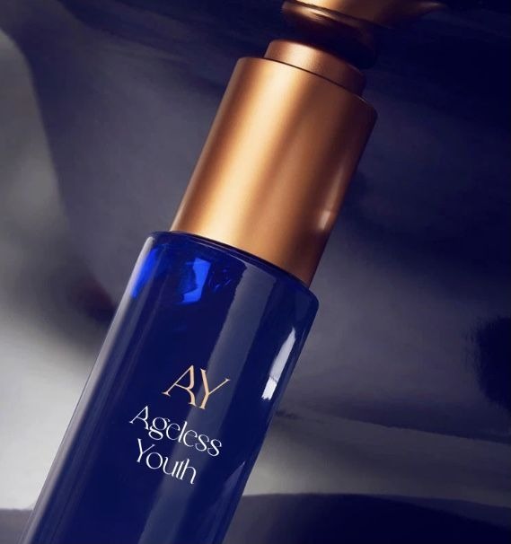 Elegancka, granatowa buteleczka serum 'AY Ageless Youth' z złotą pompką na błyszczącym, ciemnym tle. Minimalistyczny design i luksusowy charakter produktu.