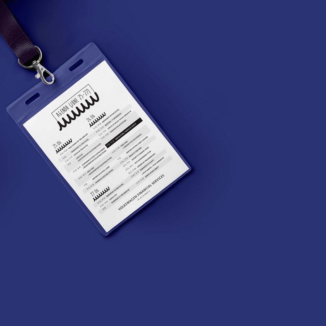 Identyfikator z agendą konferencji Volkswagen Financial Services, z datami 25-27 czerwca, leżący ukośnie na niebieskim tle. Widoczna smycz z logo.