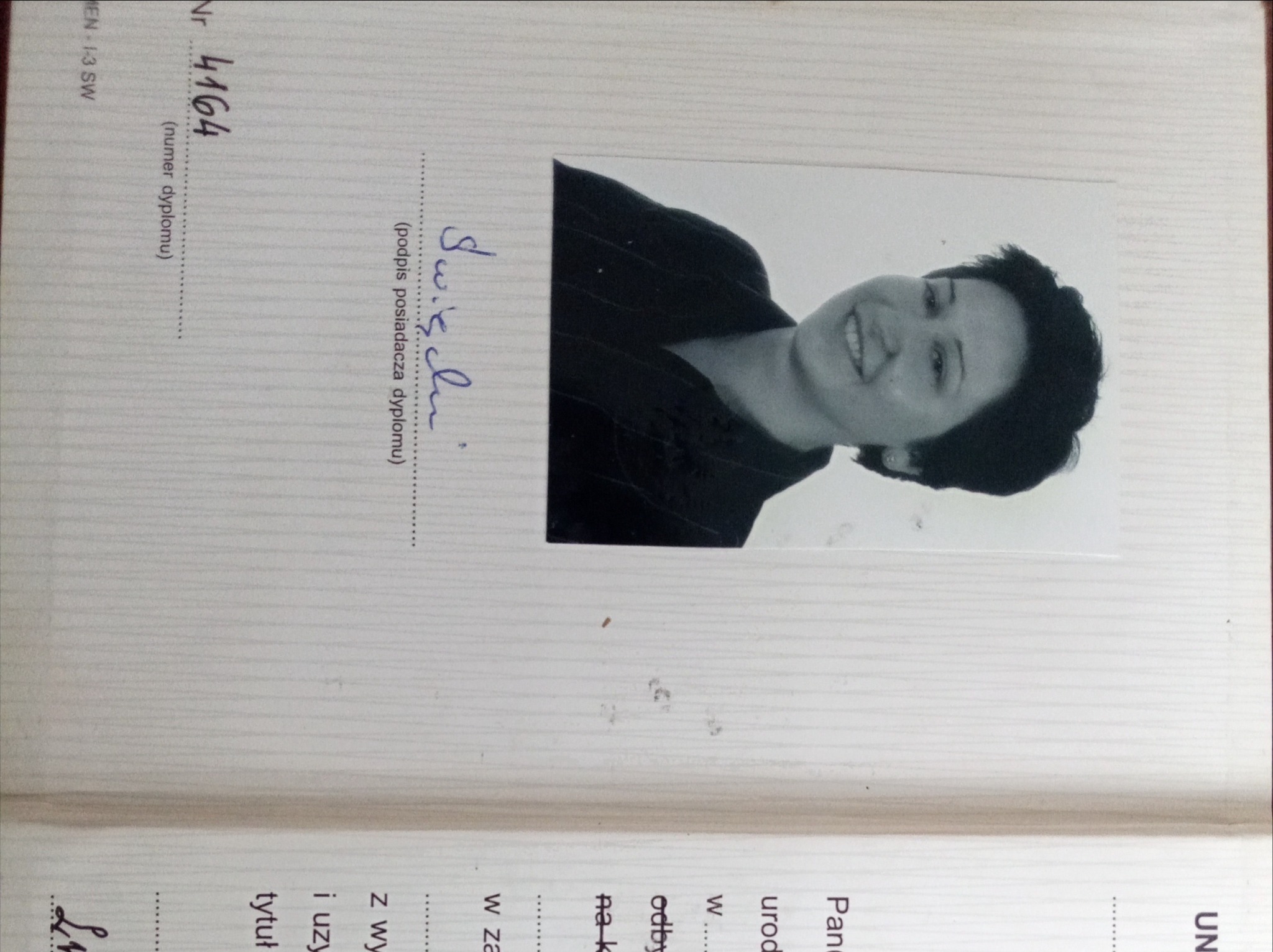 Skan dyplomu z czarno-białym zdjęciem uśmiechniętej kobiety i podpisem, leżący na otwartej książce z tekstem.