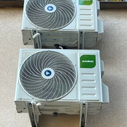 JANCZAR.BIZ DOMINIK JANCZAR - Dwa klimatyzatory Kaisai zamontowane na elewacji budynku w Stronie. Widoczne detale montażowe i okno w tle. Instalacja klimatyzacji.