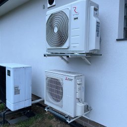 JANCZAR.BIZ DOMINIK JANCZAR - Dwa klimatyzatory Rotenso i Mitsubishi zamontowane na elewacji budynku, widoczne przewody i elementy instalacji. Zewnętrzna jednostka klimatyzacji.