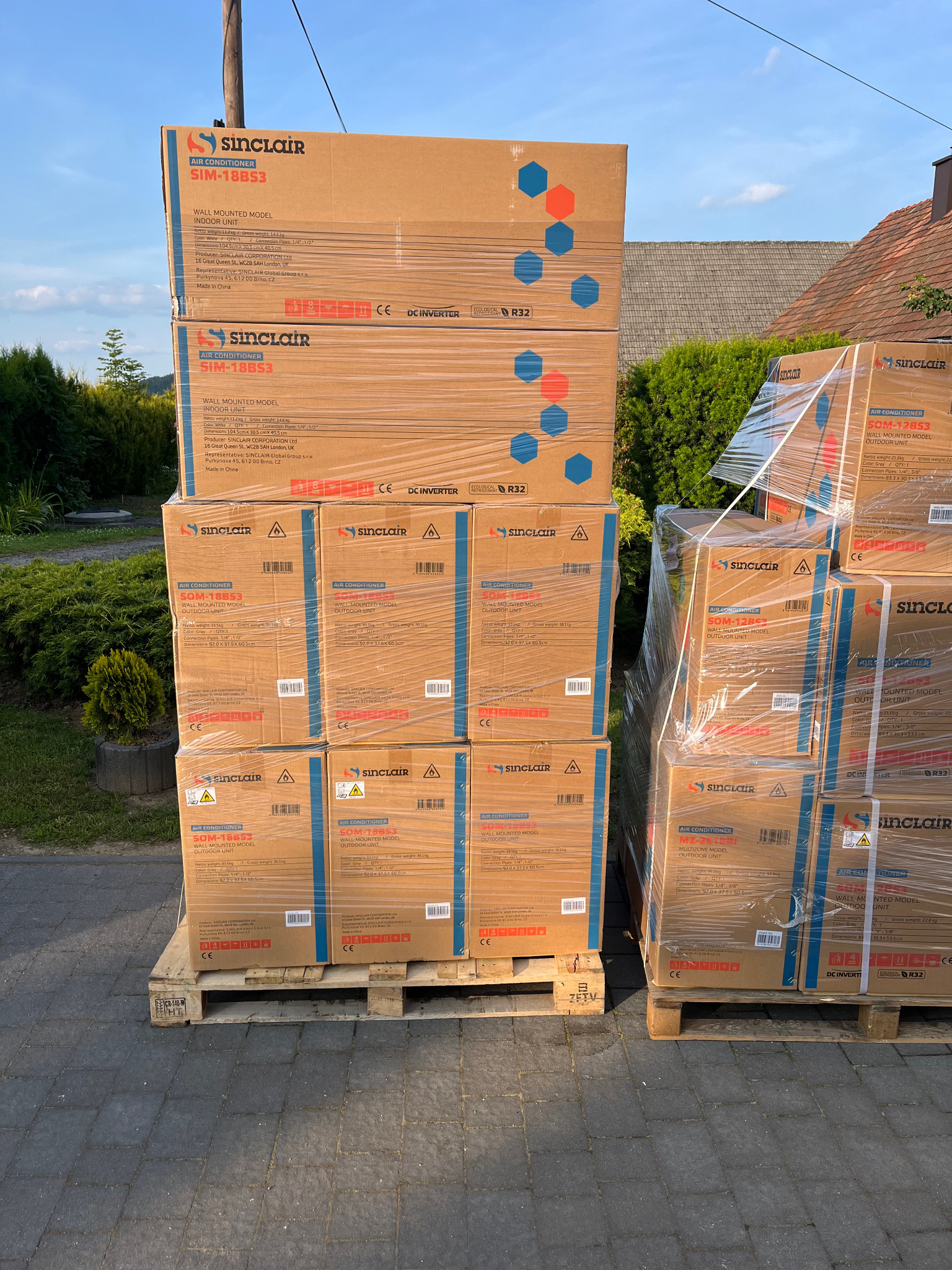 Paleta zafoliowanych kartonów klimatyzatorów Sinclair różnych modeli (SIM-18BS3, SOM-18BS3, SOM-12BS3, MZ-2612) na zewnątrz, gotowych do montażu.