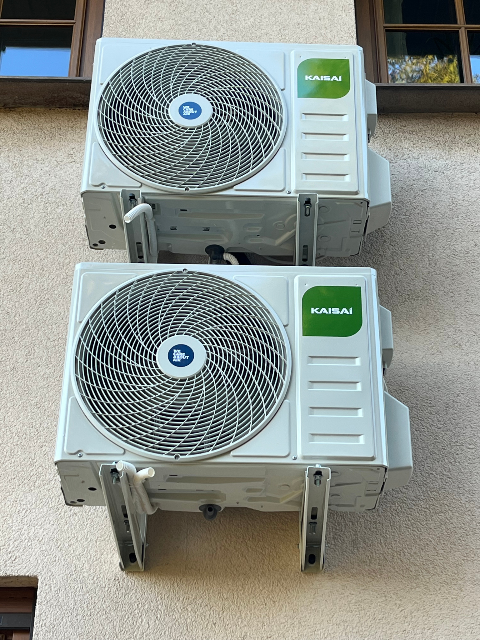Dwa klimatyzatory Kaisai zamontowane na elewacji budynku w Stronie. Widoczne detale montażowe i okno w tle. Instalacja klimatyzacji.