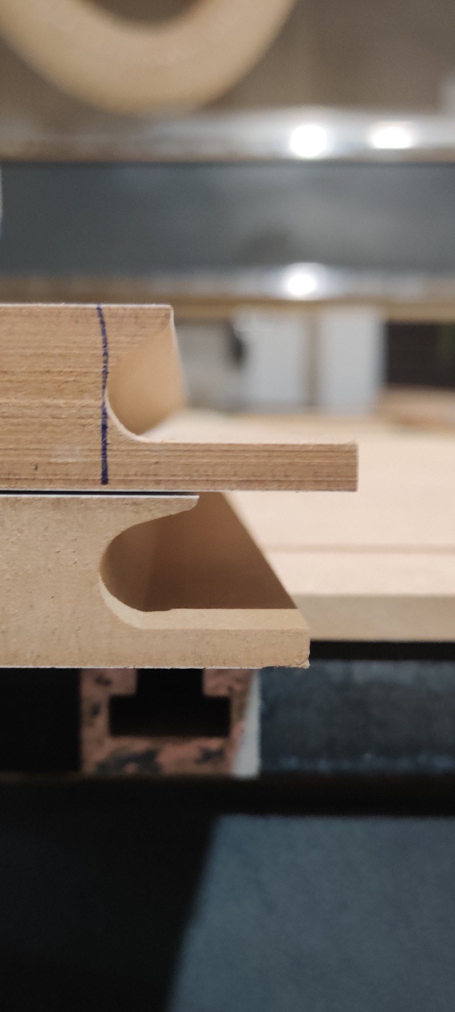 Zbliżenie na frezowane elementy drewniane z widocznymi śladami obróbki CNC i niebieskim oznaczeniem, ułożone warstwowo.