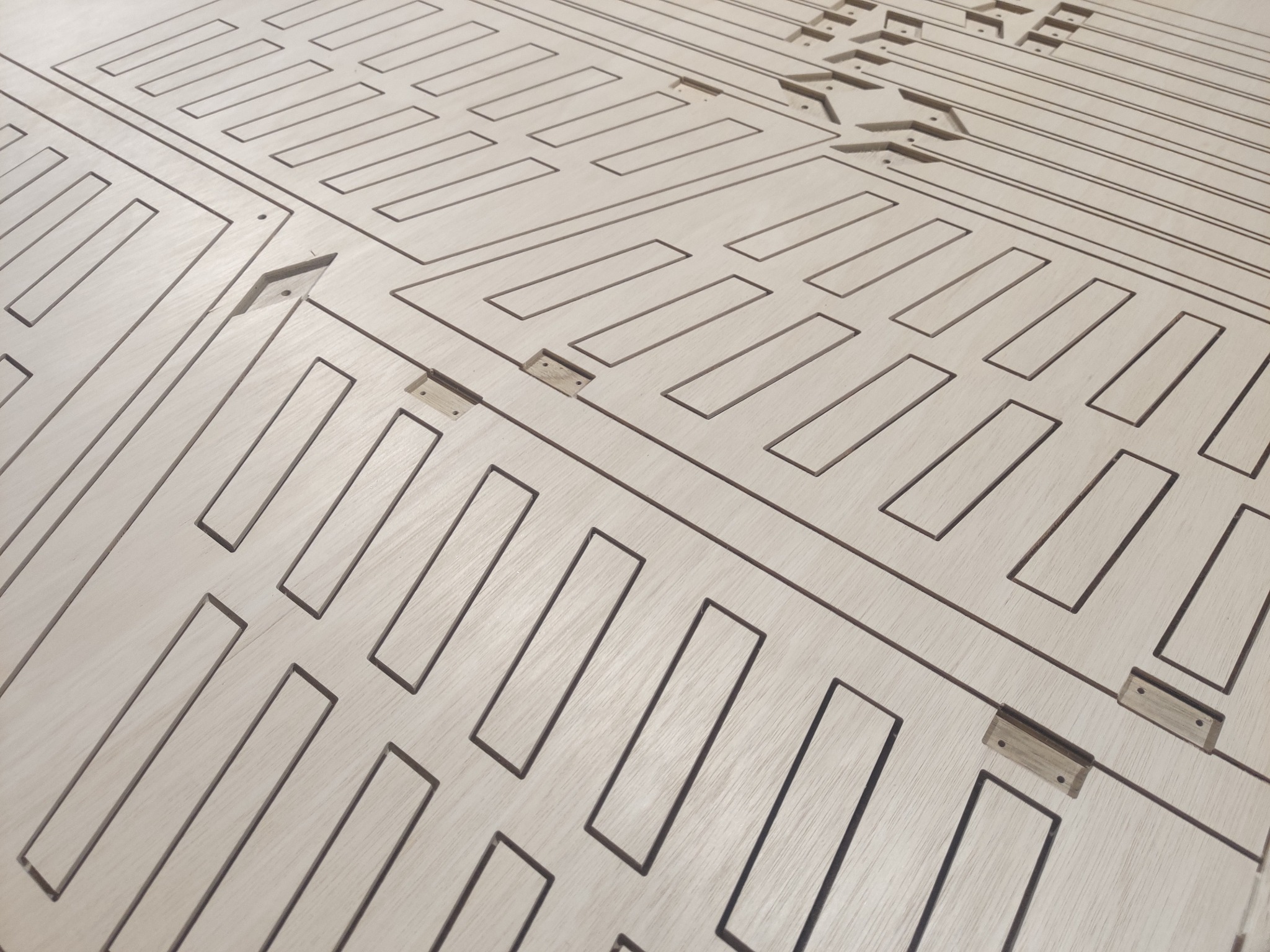 Płyta z jasnego drewna z precyzyjnie wyciętymi, prostokątnymi wzorami i małymi otworami, prawdopodobnie element konstrukcyjny wyprodukowany metodą CNC.