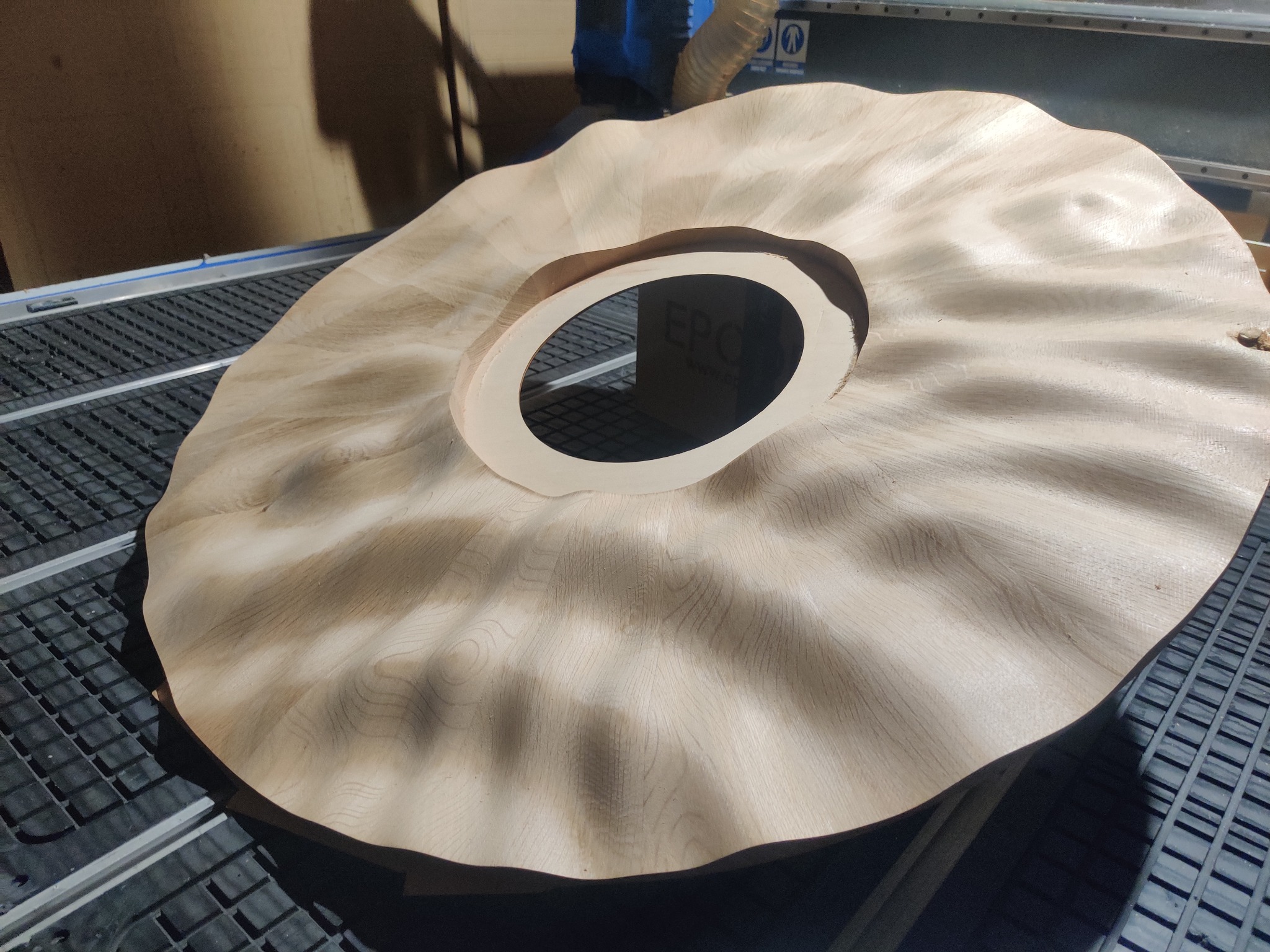 Drewniany, falisty element dekoracyjny z otworem centralnym, obrabiany na maszynie CNC, widoczne ślady frezowania i faktura drewna.