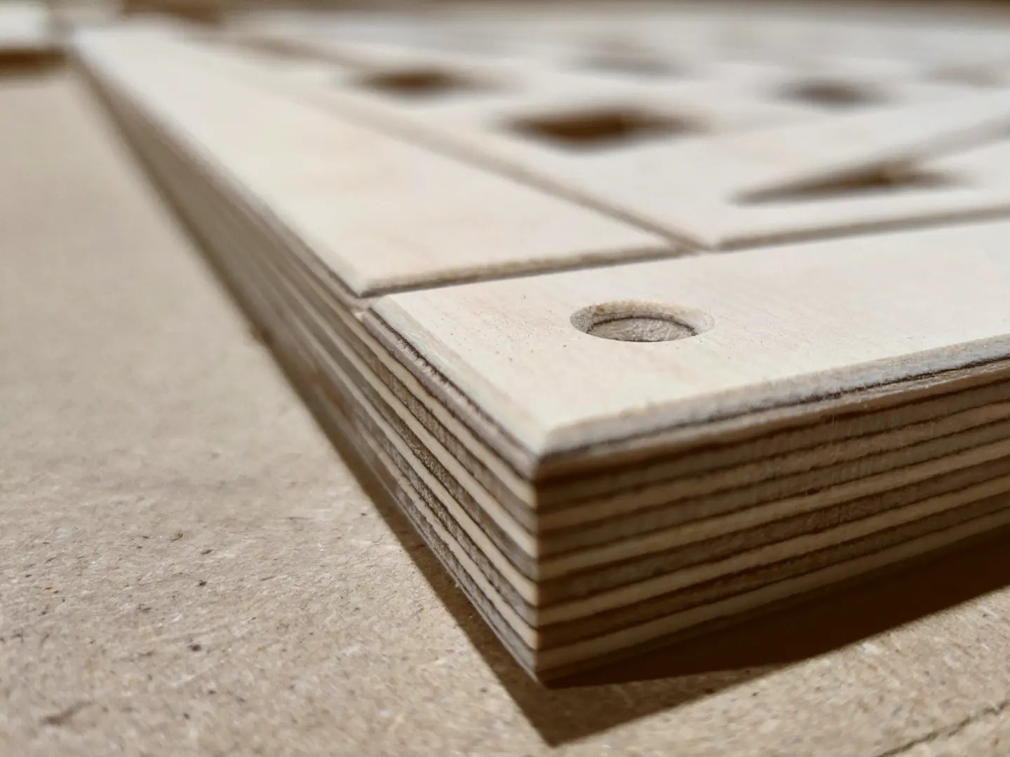 Krawędź wielowarstwowej płyty drewnianej z wyciętymi otworami i kwadratowymi wgłębieniami, widoczne słoje drewna, surowy materiał przed obróbką.