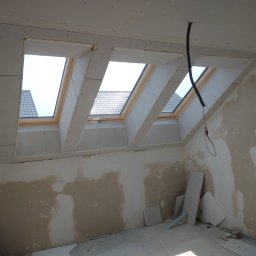 KS-BUD USŁUGI OGÓLNOBUDOWLANE KRZYSZTOF SZMAJ - Poddasze z trzema oknami dachowymi w trakcie montażu płyt kartonowo-gipsowych. Widoczne fragmenty łat i niedokończone ściany.