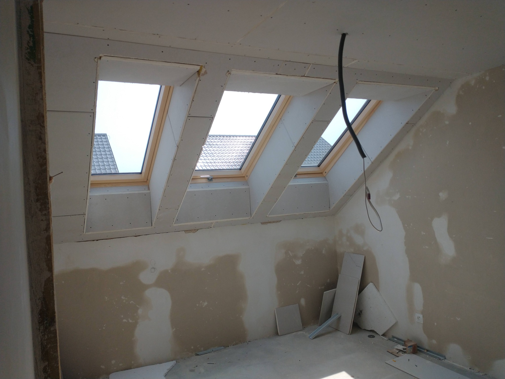 Poddasze z trzema oknami dachowymi w trakcie montażu płyt kartonowo-gipsowych. Widoczne fragmenty łat i niedokończone ściany.