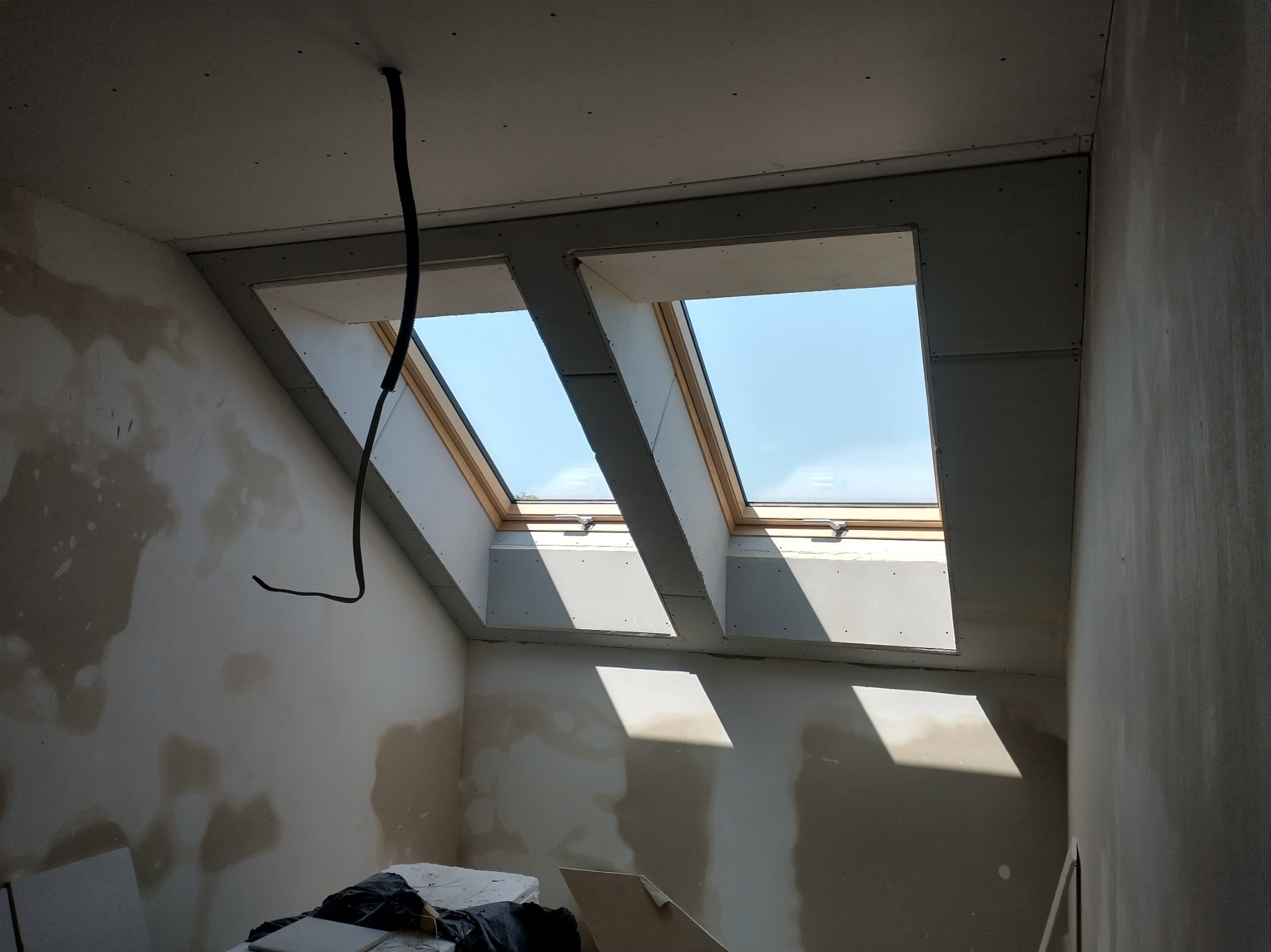 Poddasze w trakcie wykańczania: zamontowane płyty karton-gips wokół okien dachowych, ściany częściowo wyszpachlowane, widoczne przewody elektryczne.