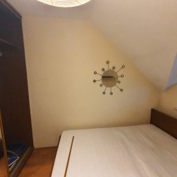 martin zych - Pokój z łóżkiem z brązowym zagłówkiem, szafą z lustrem, zegarem w stylu retro na ścianie i oknem w skosie dachu.