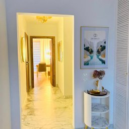 ORO Patrycja Andrzejczak-Solarz - Wnętrze salonu z marmurową podłogą, widok na korytarz, dekoracyjny stolik z wazonem i plakatem z logo firmy na ścianie.