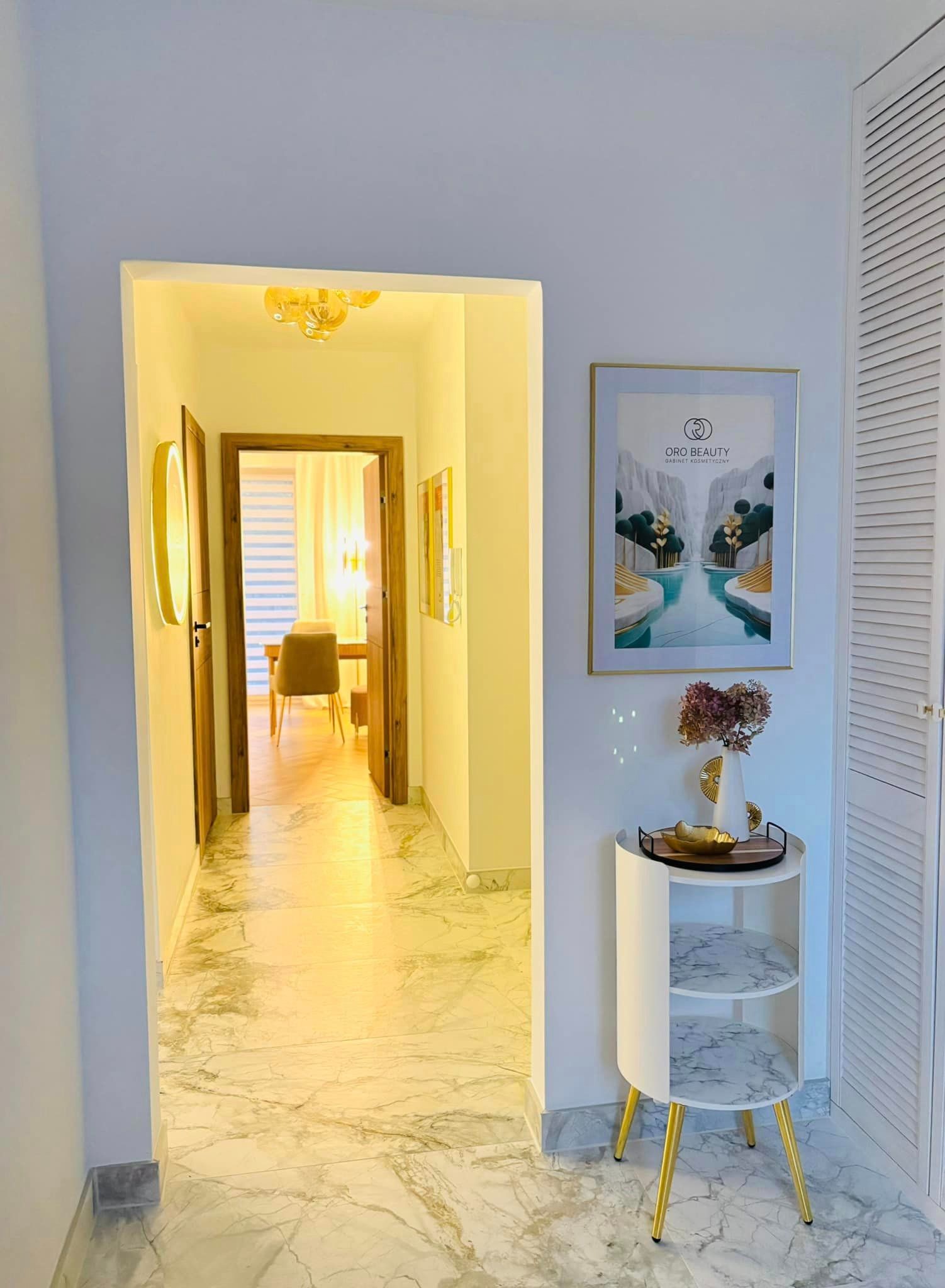 Wnętrze salonu z marmurową podłogą, widok na korytarz, dekoracyjny stolik z wazonem i plakatem z logo firmy na ścianie.