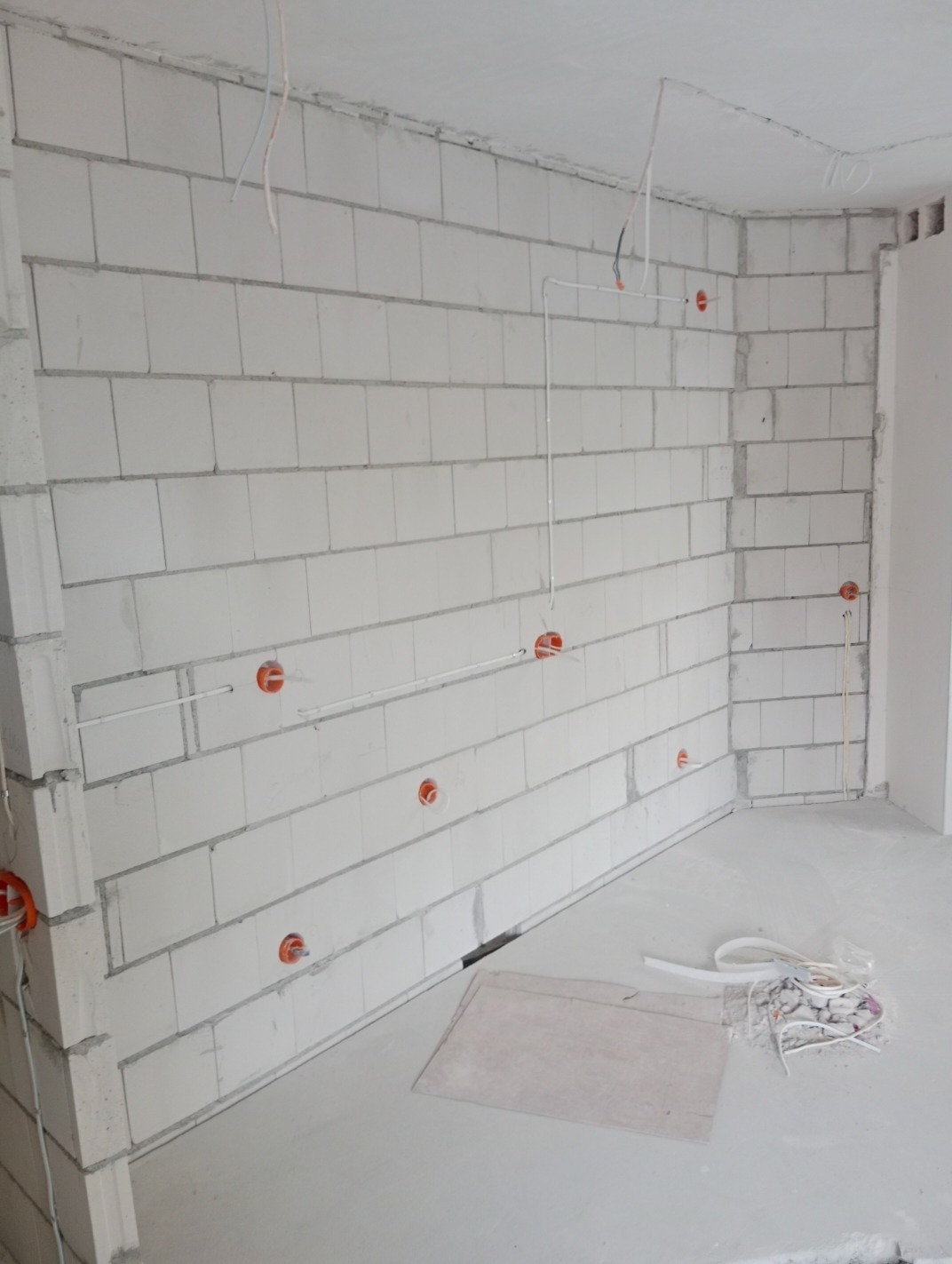 Surowa ściana z betonu komórkowego z widocznymi puszkami instalacyjnymi i przewodami elektrycznymi w trakcie montażu. Na podłodze leżą fragmenty kabli i karton.