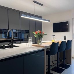 PROGRES SPÓŁKA Z OGRANICZONĄ ODPOWIEDZIALNOŚCIĄ - Nowoczesna kuchnia z czarnymi, lakierowanymi frontami szafek, jasnym blatem, drewnianą wyspą z trzema hokerami i wiszącą lampą liniową.