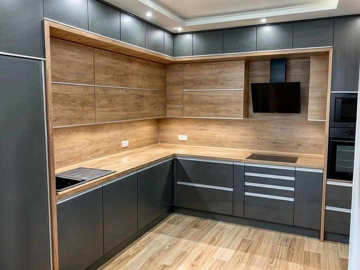 Nowoczesna kuchnia z szarymi szafkami na wysoki połysk i drewnianymi frontami górnych szafek, drewniany blat, płyta indukcyjna i czarny okap.