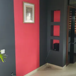 Dwukolorowe ściany: grafit i koralowa czerwień. Wnęki w ścianie z głośnikiem. Obraz w ramie. Gniazdko elektryczne. Płytki podłogowe. Nowoczesne wykończenie wnętrza.