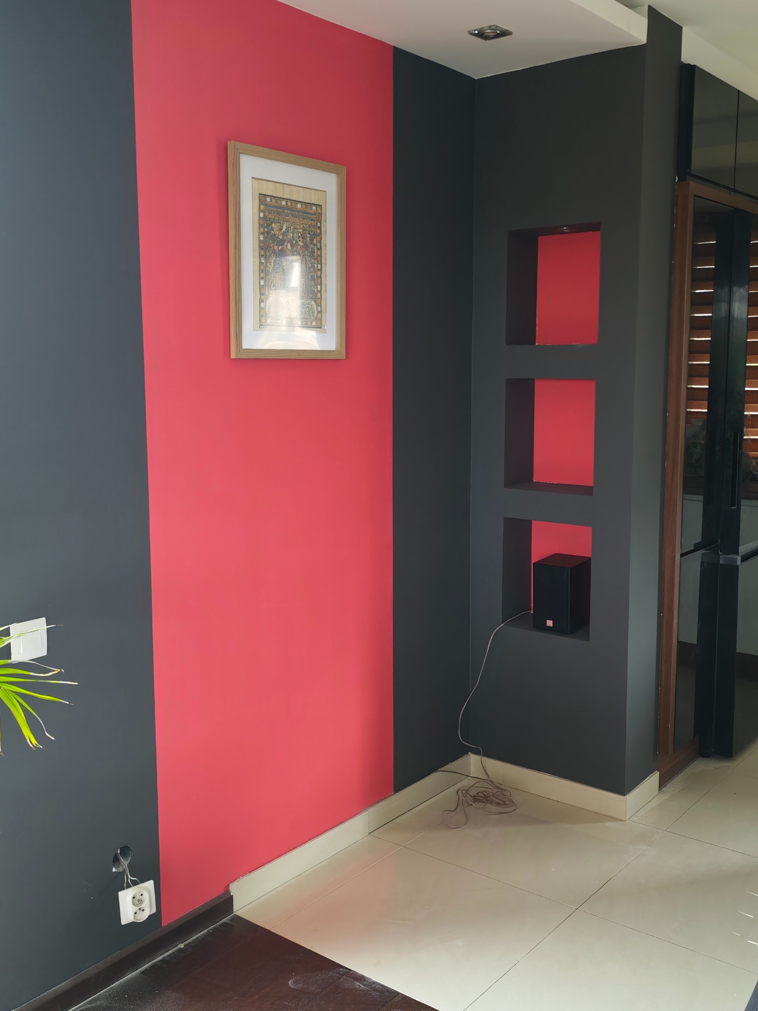 Dwukolorowe ściany: grafit i koralowa czerwień. Wnęki w ścianie z głośnikiem. Obraz w ramie. Gniazdko elektryczne. Płytki podłogowe. Nowoczesne wykończenie wnętrza.