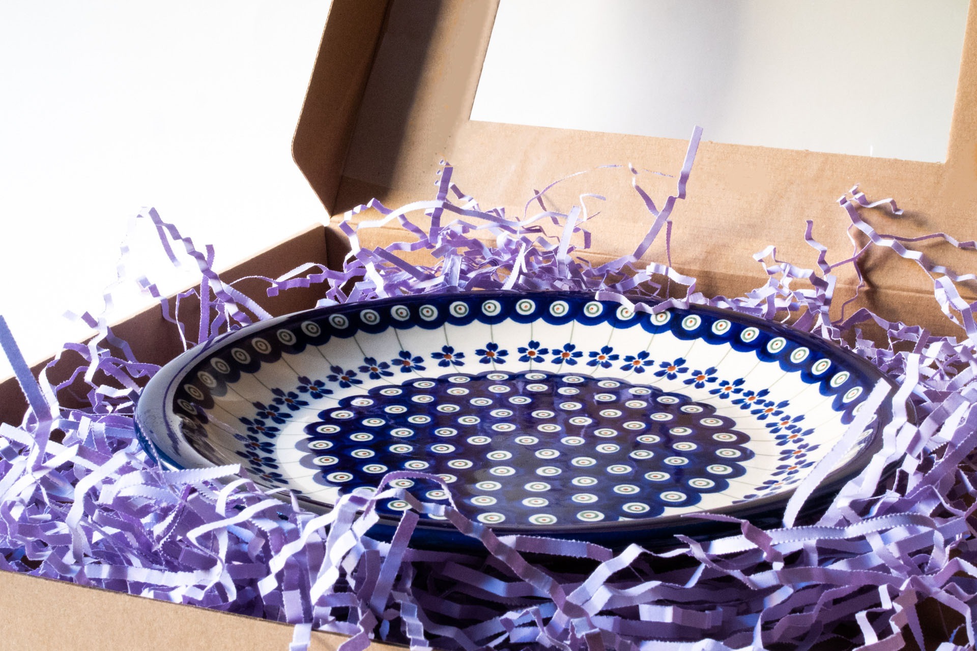 Ręcznie malowany talerz ceramiczny w niebiesko-białe wzory, zapakowany w kartonowe pudełko z fioletowym wypełniaczem papierowym.