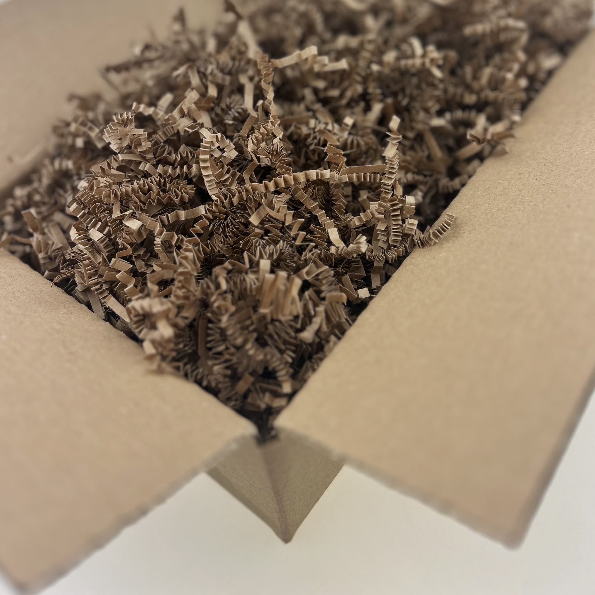 Otwarty karton wypełniony brązowym, karbowanym wypełniaczem papierowym, widok z góry.