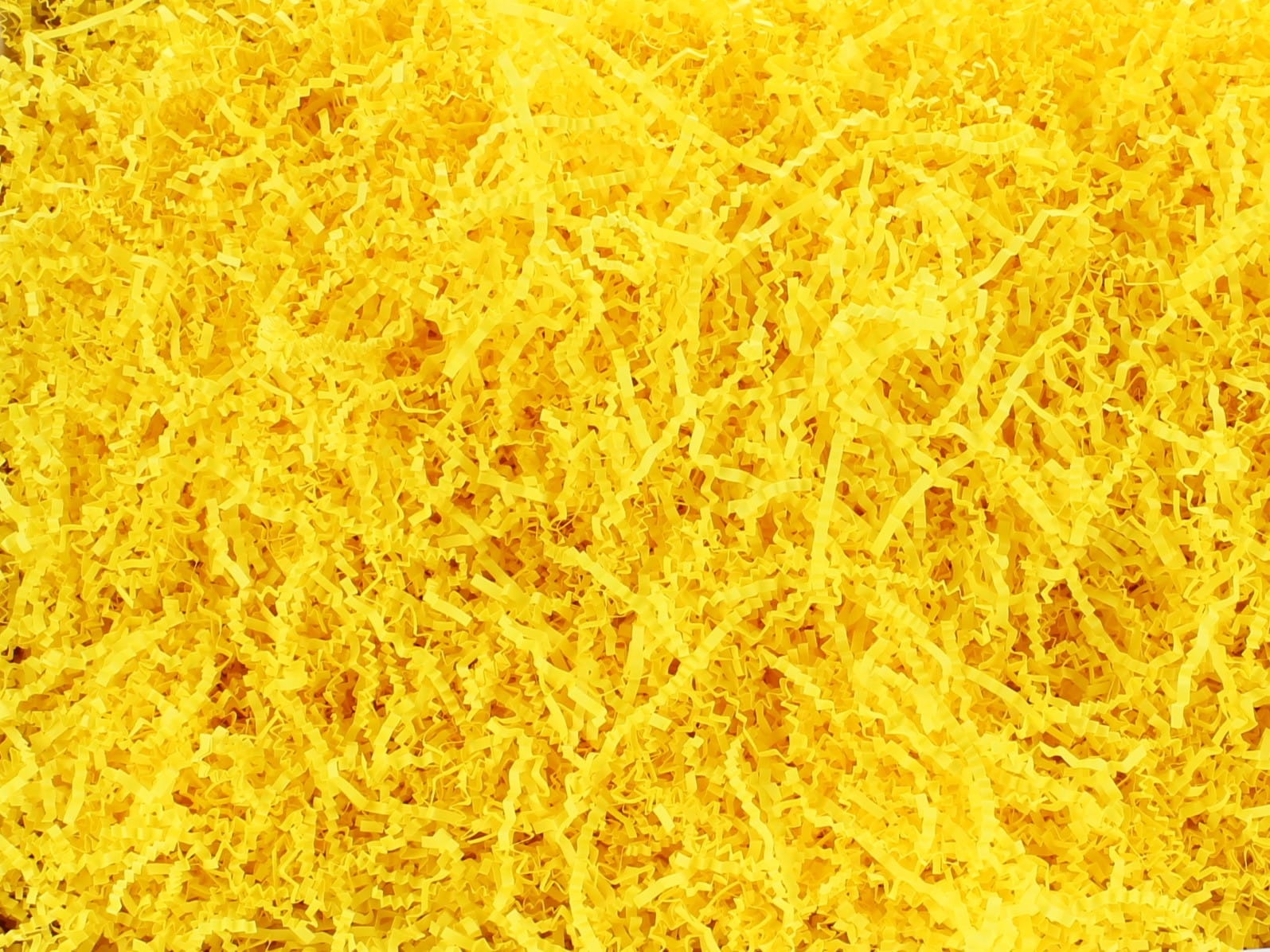 Jasnożółte, pocięte paski papieru, wypełniacz do paczek, widoczne w zbliżeniu, tworzące teksturę.