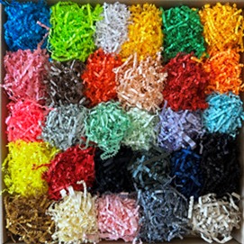 Kwadratowe pudełko wypełnione kolorową, pociętą bibułą dekoracyjną w różnych odcieniach, tworzącą efekt wizualnego bogactwa i różnorodności.