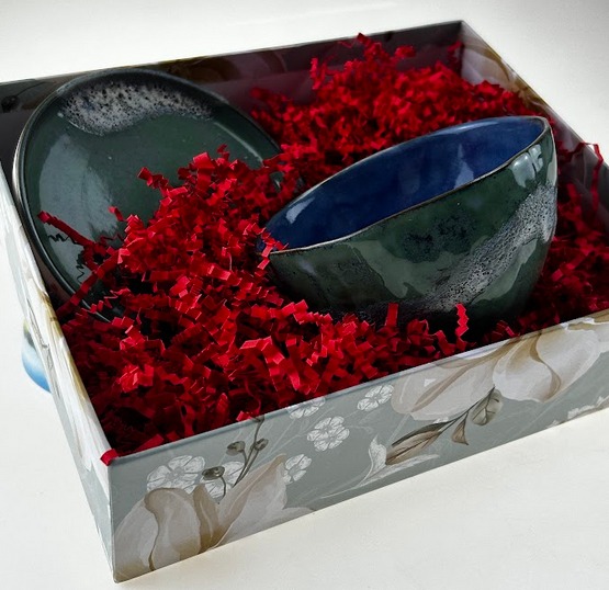 Ceramiczna miska i talerz w odcieniach zieleni i granatu, ułożone w pudełku wyłożonym czerwoną rafią, pudełko z motywem kwiatowym.