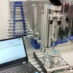 Pomiar momentu obrotowego za pomocą klucza dynamometrycznego i specjalistycznego stanowiska pomiarowego z laptopem rejestrującym dane, na tle ściany z narzędziami.