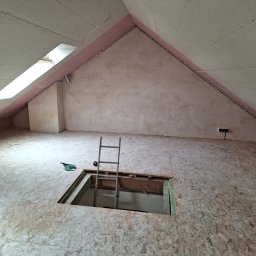 M&D BUD - Poddasze w trakcie adaptacji: ściany przygotowane do dalszych prac, widoczne płyty OSB na podłodze z otworem i przystawioną drabiną, okno dachowe w skosie.